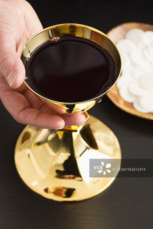 基督教圣餐，男子手持盛有酒的金杯，餐盘上盛有圣餐饼图片素材