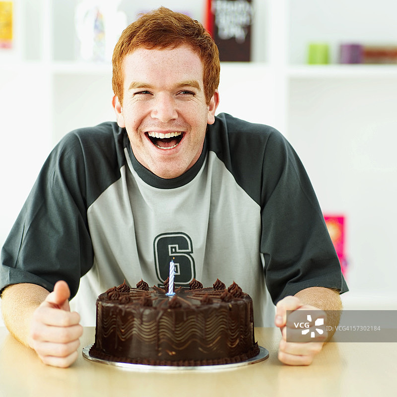 一个年轻人的肖像与生日蛋糕在他面前微笑图片素材