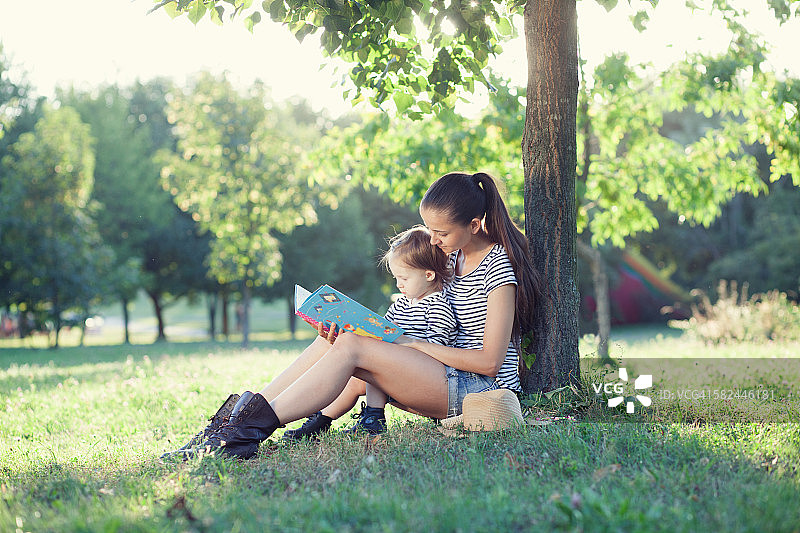 年轻时尚的母亲和蹒跚学步的孩子阅读书在g图片素材