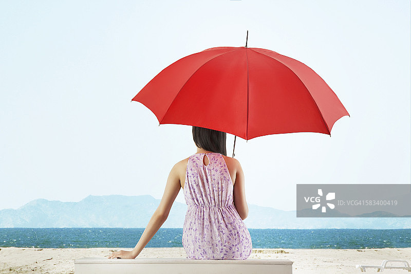 拿着伞坐在大海前的女人图片素材