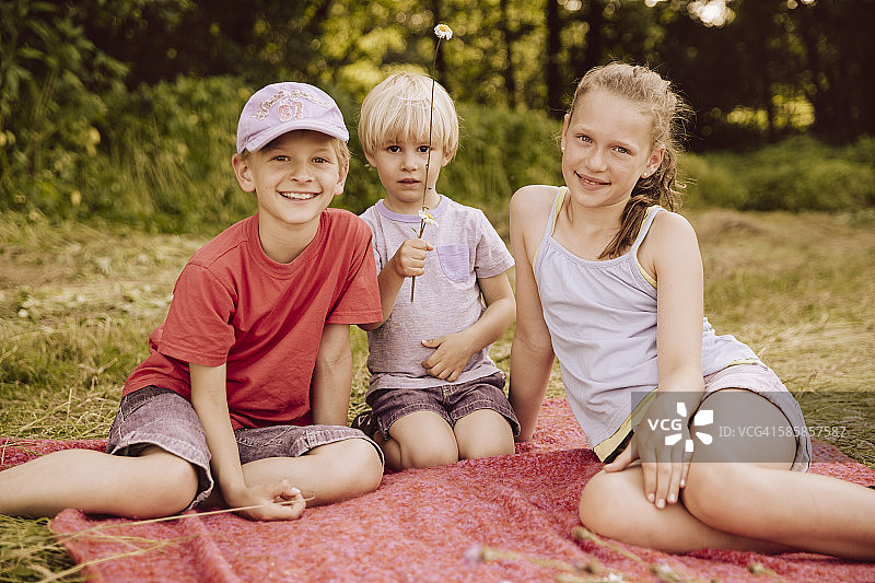 三个孩子坐在草地上的毯子上图片素材