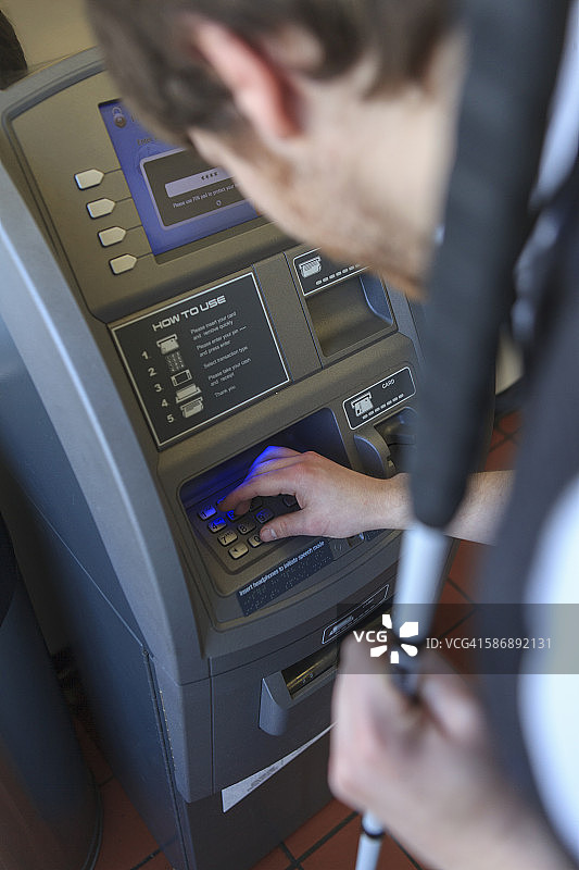一个年轻的盲人拄着拐杖使用银行ATM机图片素材