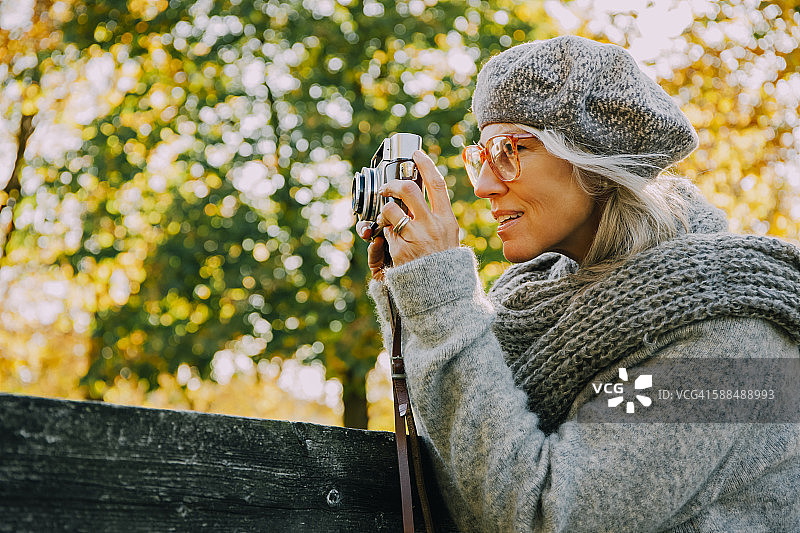 一个女人在秋天的公园里用旧相机拍照图片素材