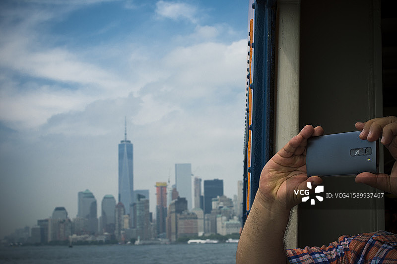 美国，纽约市，游客用智能手机拍摄曼哈顿天际线和东河的景色图片素材