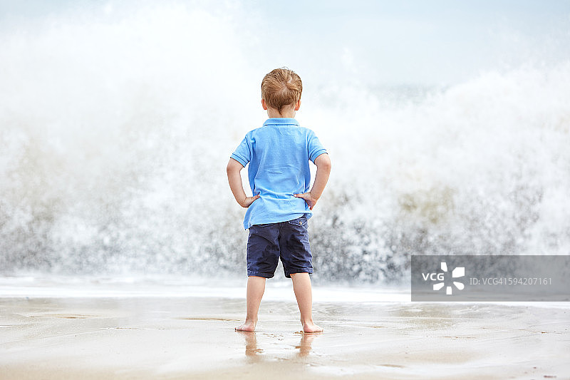 小男孩看着海滩上的海浪图片素材
