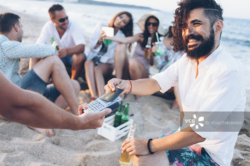在海滩上喝啤酒刷信用卡的年轻人图片素材