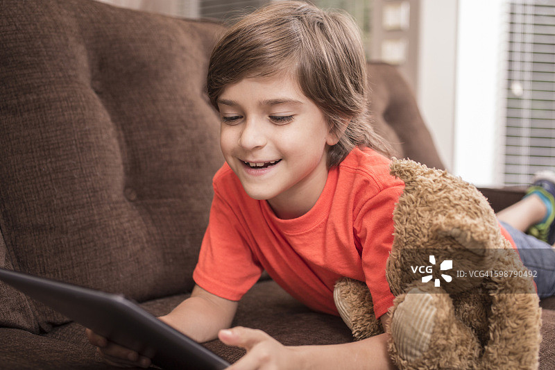 孩子在家阅读数字平板电脑与泰迪熊。图片素材