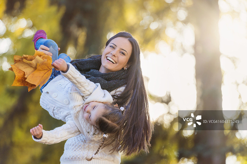 快乐母亲抱着女儿抱着秋叶图片素材