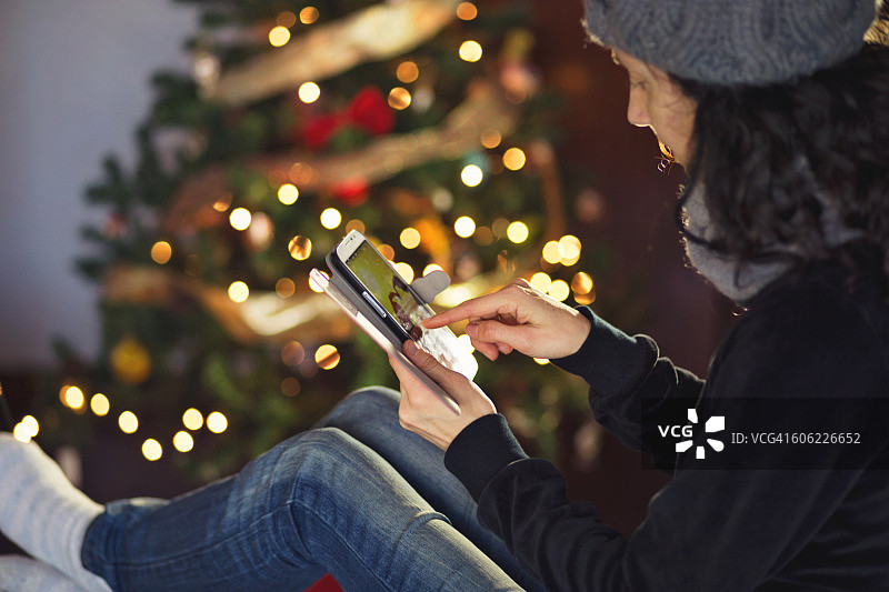 一名女子在圣诞树旁使用智能手机。图片素材