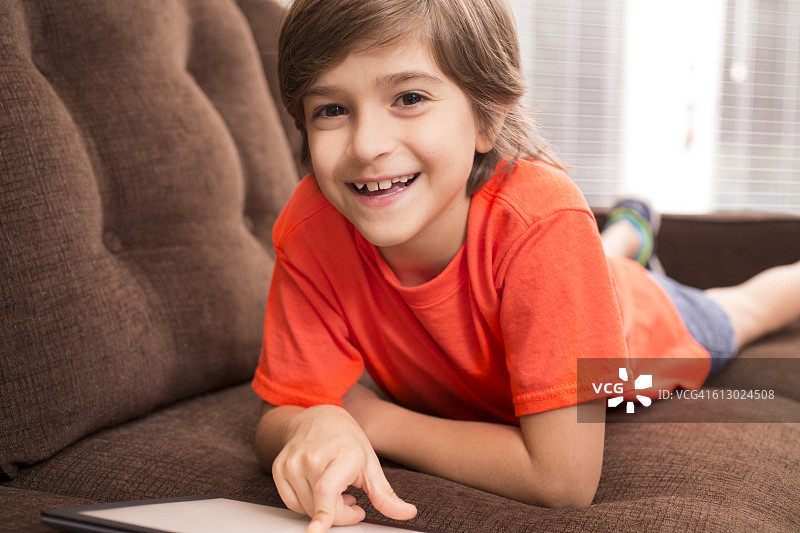 孩子在家看数字平板电脑在沙发上。图片素材