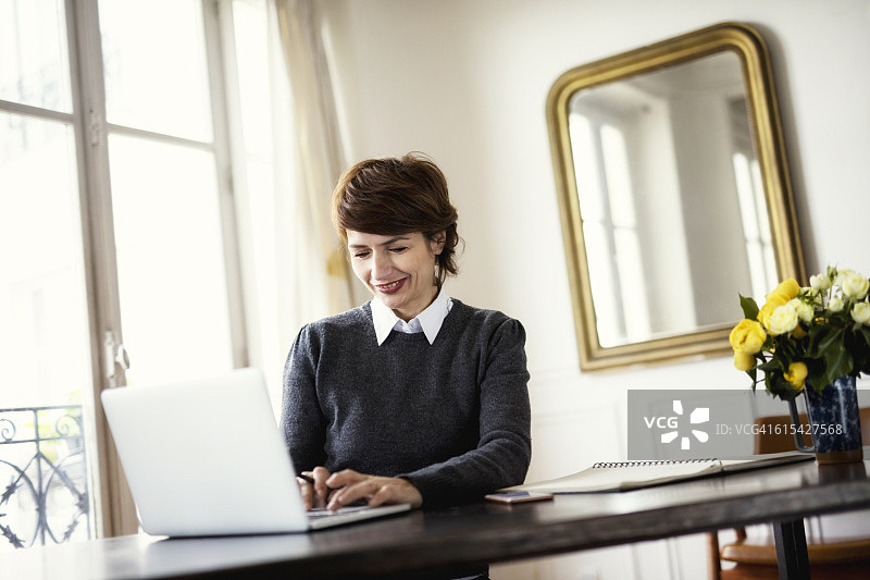 微笑的女人使用笔记本电脑在桌子靠窗图片素材