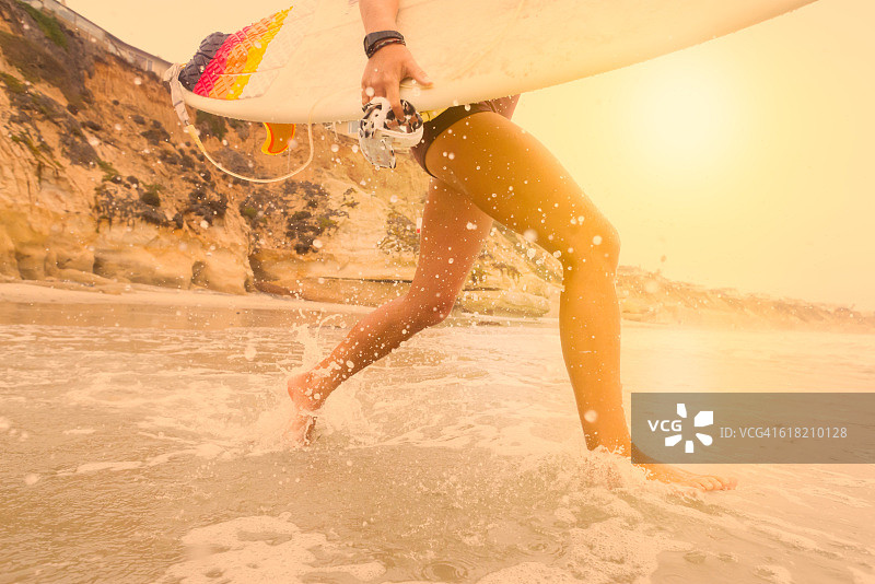 低角度女子冲浪者在日落时跑进海洋图片素材