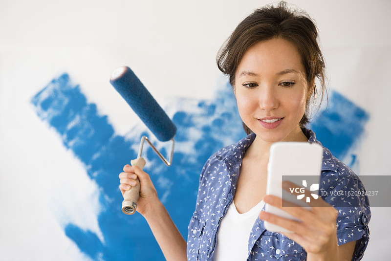 混血妇女使用手机和油漆墙壁图片素材