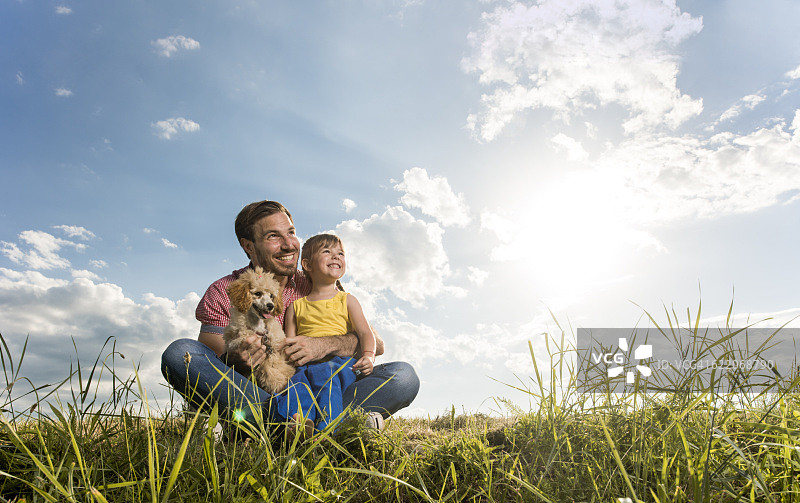 慈爱的父女和他们的狗在草地上。图片素材