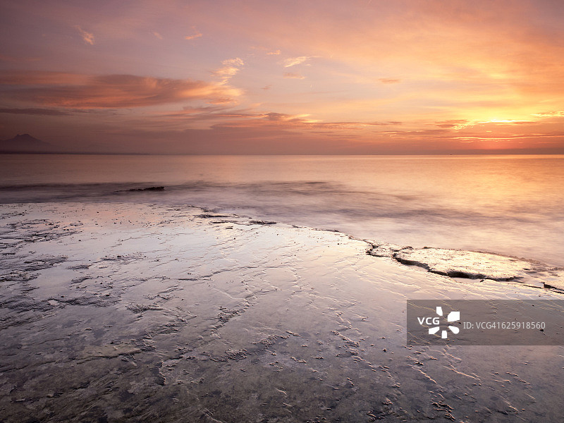 黎明的第一缕阳光染成了橘色，这是一片岩石和波浪起伏的海岸图片素材