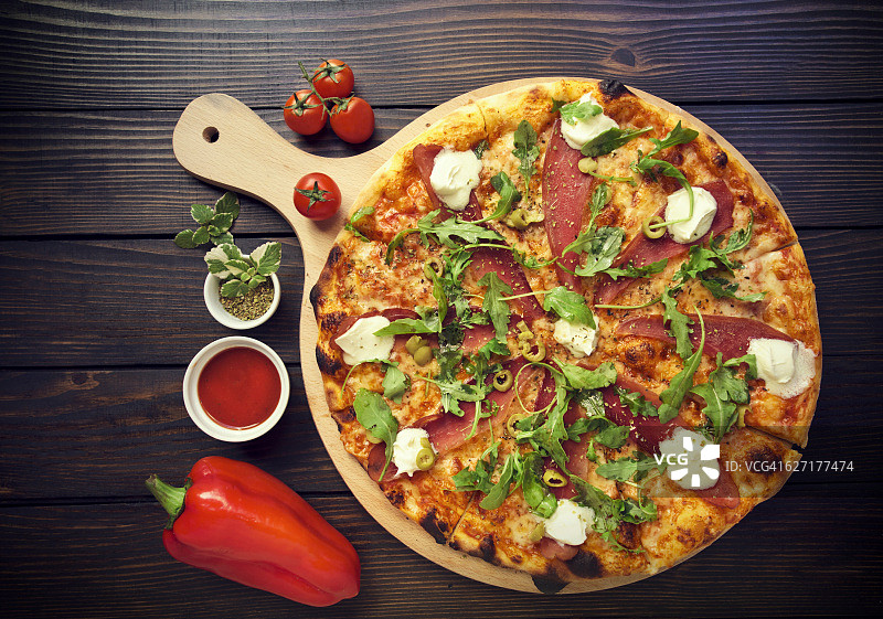 木桌上放着意大利腊肠、橄榄和罗勒的乡村披萨图片素材