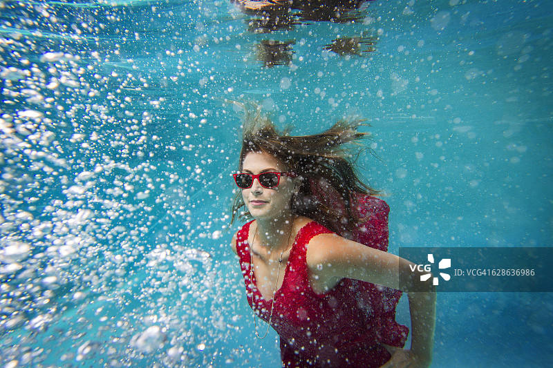 一名身穿红色连衣裙的女模特在加州圣地亚哥的游泳池里水下的肖像。图片素材