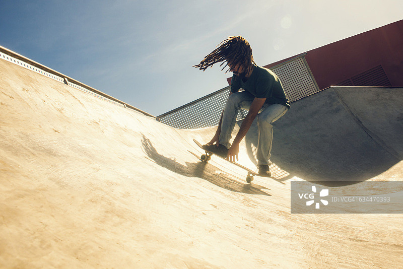 一个留着长发绺的年轻人在滑板公园玩滑板图片素材