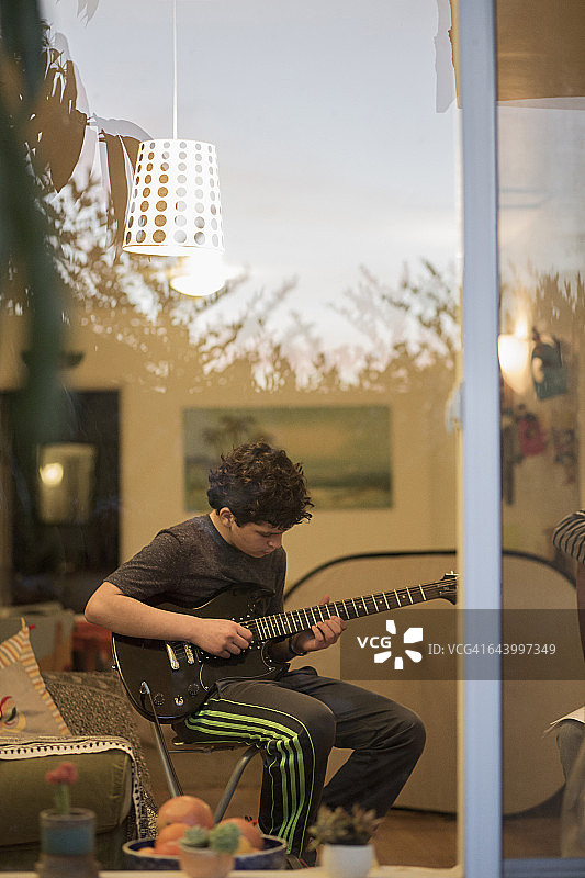 一个白人男孩在客厅弹吉他图片素材