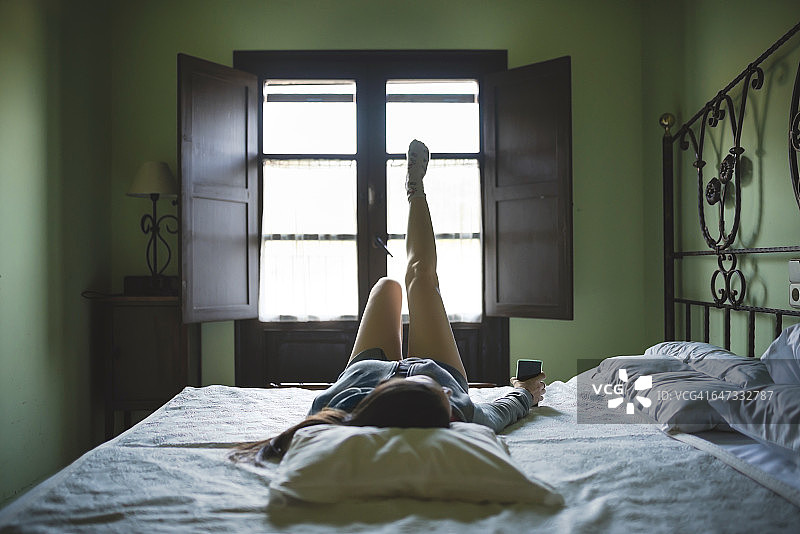 放松的女人躺在床上用智能手机图片素材