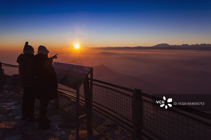 在瑞士提契诺的杰诺索山，一对徒步旅行的老夫妇在日落时眺望山谷的薄雾图片素材