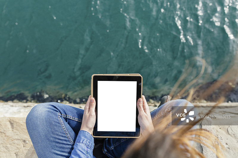 年轻女子坐在码头上使用数码平板电脑图片素材