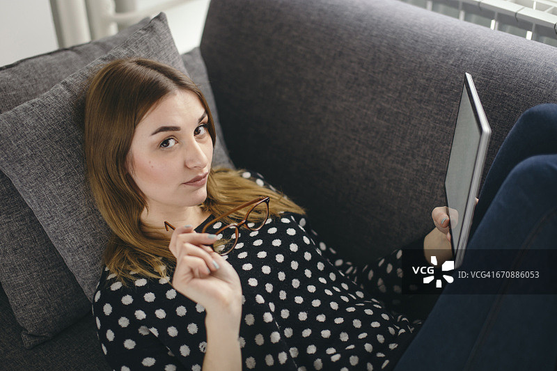 一名年轻女子用平板电脑躺在沙发上的肖像图片素材