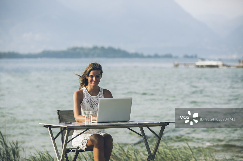 意大利，加尔达湖，一个年轻女子坐在桌子旁，拿着笔记本电脑图片素材