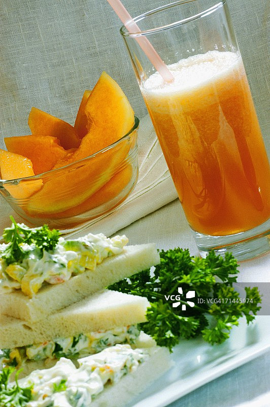 特写的一杯果汁和一碗水果沙拉与一个三明治在托盘上图片素材