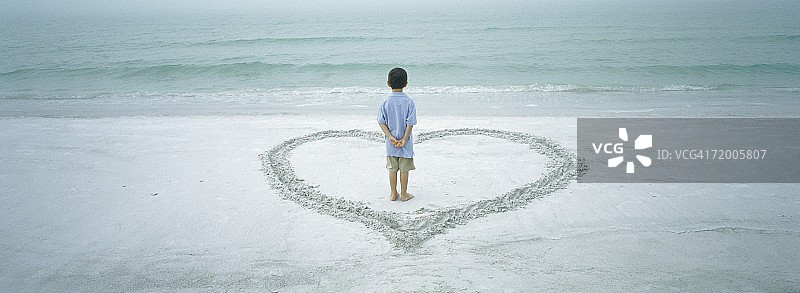 男孩站在沙滩上画的心里面，后视图图片素材