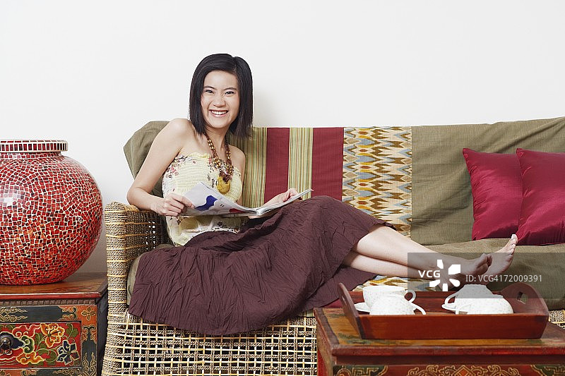 一个年轻女人的肖像坐在沙发上，拿着一本杂志图片素材