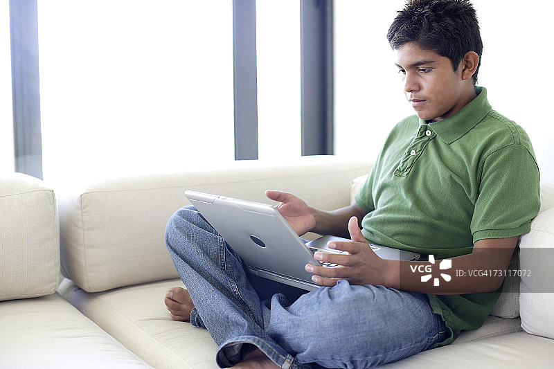 少年(15-17岁)在沙发上使用笔记本电脑图片素材