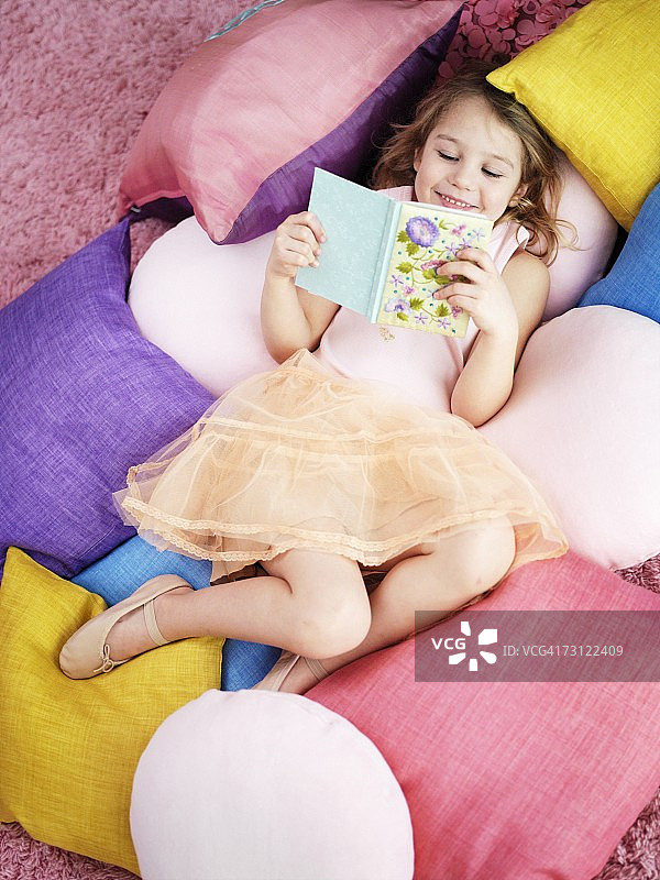 一个女孩在一堆枕头上看书。图片素材