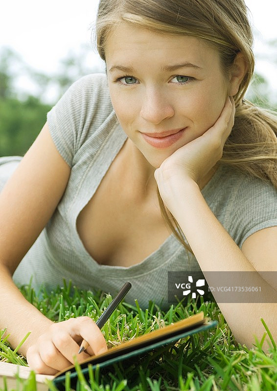 年轻女子斜倚在草地上，拿着笔记本和铅笔，还有肖像图片素材