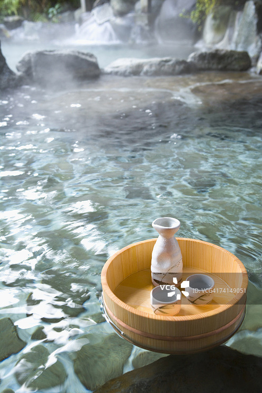 一个日本户外温泉浴，米酒瓶子和杯子在一个浮动的浴缸，高角度视图图片素材