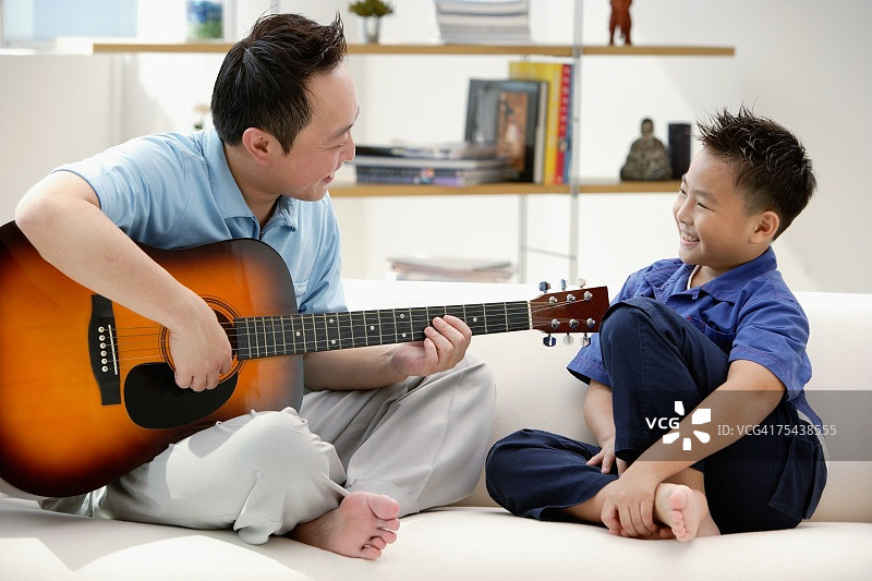 父子俩坐在沙发上，爸爸弹吉他图片素材