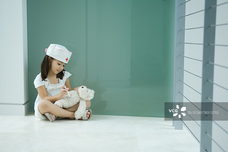戴护士帽的小女孩正在打泰迪熊图片素材