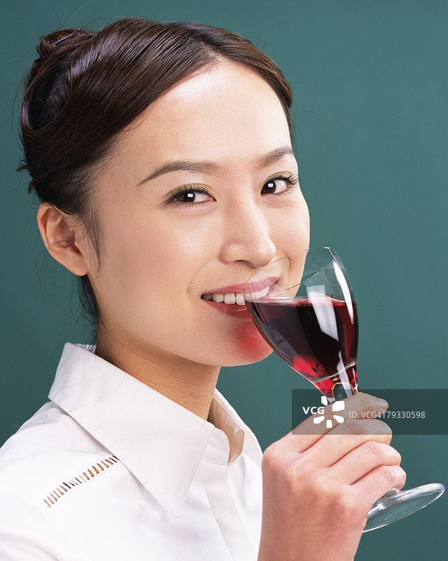一个女人喝着红酒，微笑着，看着相机，侧视图图片素材
