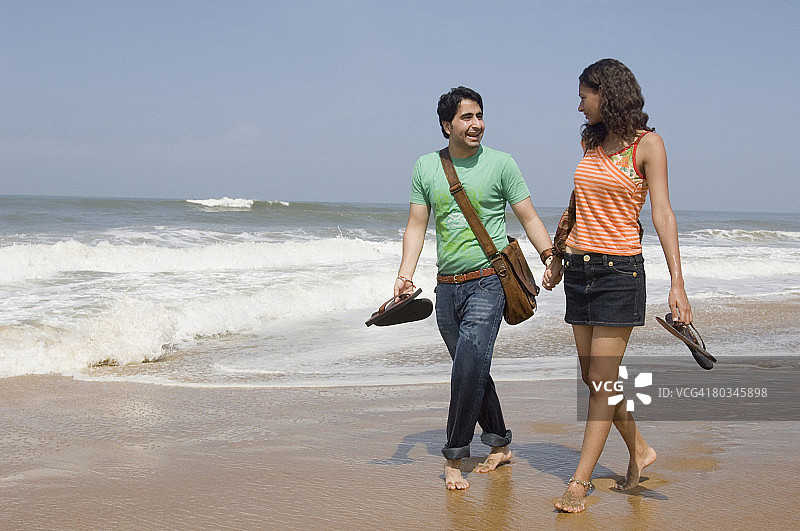 一对年轻夫妇手牵着手在海滩上散步图片素材