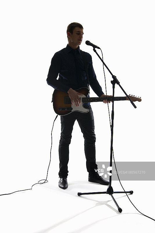 摄影棚拍摄了一名男子对着麦克风唱着歌，弹着电吉他图片素材