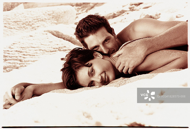 年轻夫妇躺在沙滩上，微笑着，肖像(色调B&W)图片素材