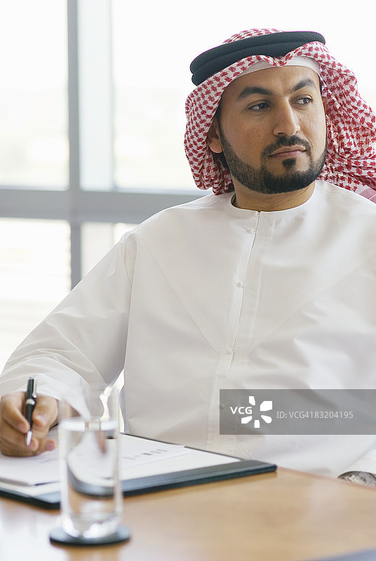 身着传统中东服饰的男子坐在桌旁的肖像，阿联酋迪拜图片素材