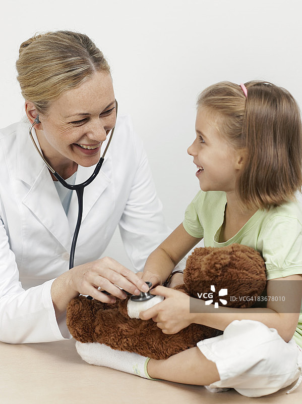 女儿科医生正在检查一个女孩的泰迪熊图片素材