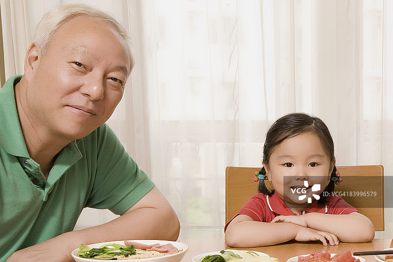 一个成熟的男人和他的孙女坐在餐桌旁的肖像图片素材