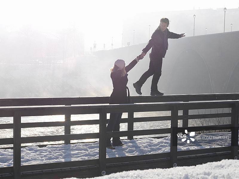 男子在桥栏杆上保持平衡，女子协助图片素材