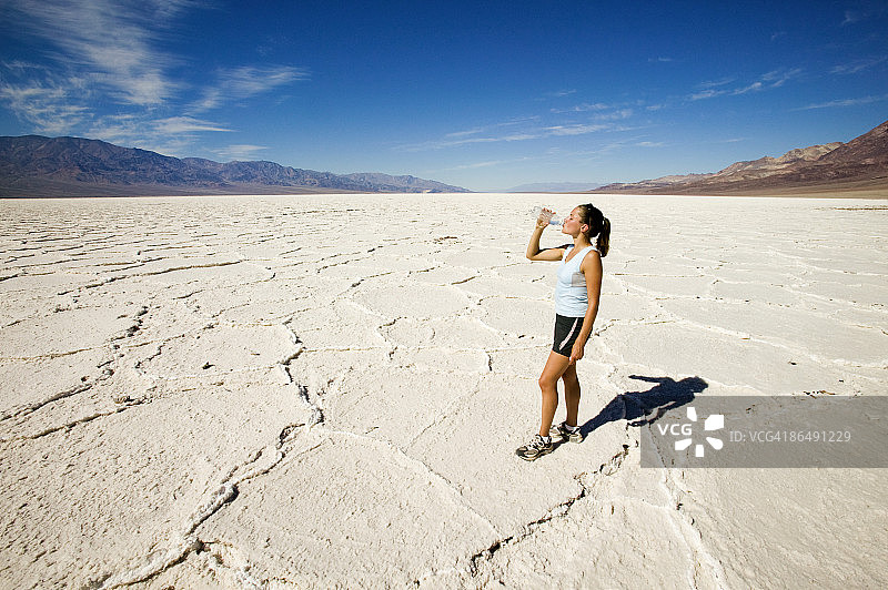 美国犹他州博纳维尔盐滩，一个女人拿着水瓶站在沙漠里图片素材