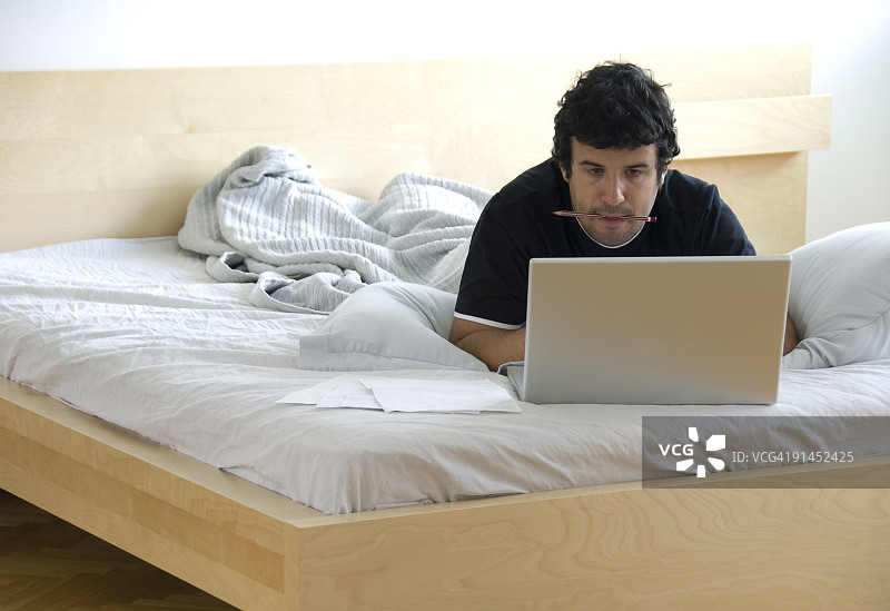 土耳其伊斯坦布尔，一名男子在床上用笔记本电脑工作图片素材