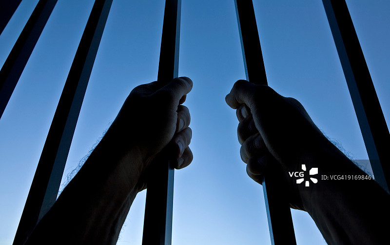 清澈的蓝天下，监狱铁栏后的双手剪影图片素材