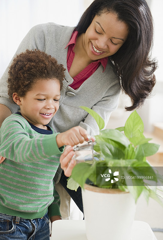 混血母亲帮助儿子浇灌植物图片素材