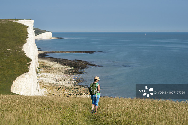 英国，欧洲，英格兰，东苏塞克斯，南唐斯国家公园，一名女子沿着比奇角附近的悬崖散步，远处可以看到七姐妹海岸线图片素材